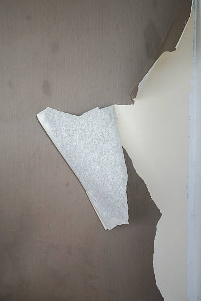 Peeling wallpaper on a wall reveals layers underneath, suggesting renovation, decay, or abstract texture background.
