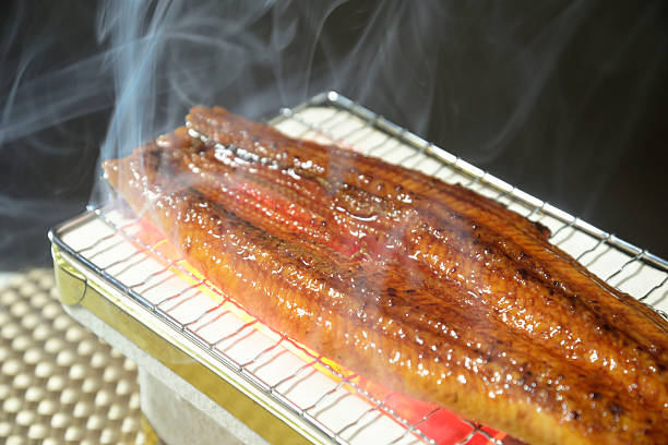 Grilled eel on a charcoal grill with smoke rising