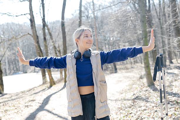 Hiker enjoying a moment of mindfulness during her trekking day, opening her arms and listening to music with headphones in the forest