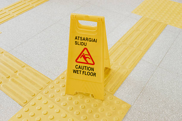 istock Yellow plastic caution sign on tactile paving for visually impaired, warning about wet floor in a public indoor space, bilingual text in Lithuanian and English 2223161636