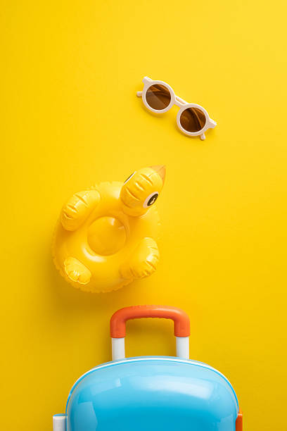 Bright vertical yellow backdrop featuring sunglasses, an inflatable duck, and a colorful suitcase, perfect for travel or summer-themed projects