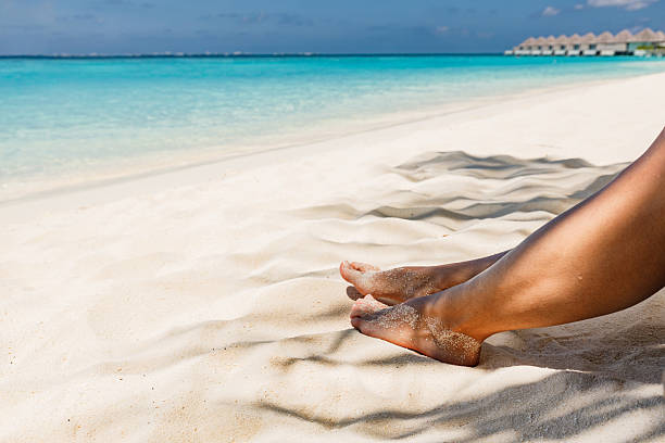 Close up of unrecognizable woman relaxing her feet in sand during summer day on the beach. Copy space.