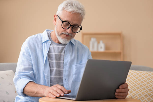 istock Senior man using laptop at wooden table indoors 2223173968