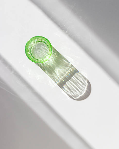 istock Top view of green colored glass mug creating vivid light reflections and caustics on white background. Transparent cup at sunlight with window shadows, summer drink concept, minimal trend, copyspace 2223174427