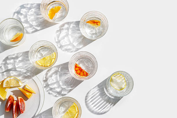 istock Fruit Infused Water in Glasses and plate with Shadows at sunlight on White background. Aesthetic Top view summer detox drink with slices of lemon and orange with sun flare from glass cups 2223174439