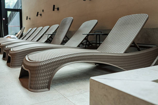 istock Curved beige wicker loungers line an indoor spa deck, creating a modern, tranquil relaxation zone beside the pool 2223175615
