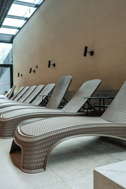 istock Curved beige wicker loungers line an indoor spa deck, creating a modern, tranquil relaxation zone beside the pool 2223175619