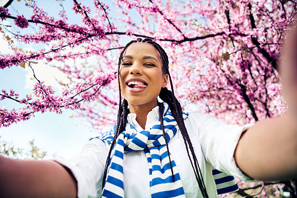 Charming woman captures cheerful selfie outdoors surrounded by blooming spring blossoms during a sunny day