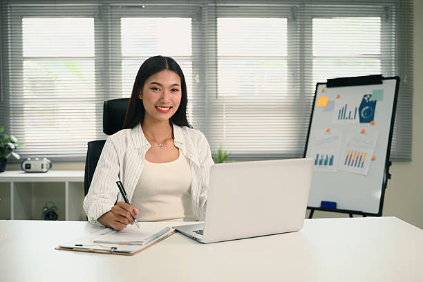 istock Portrait of young entrepreneur smiling while taking notes and using a laptop in a bright office 2223177120