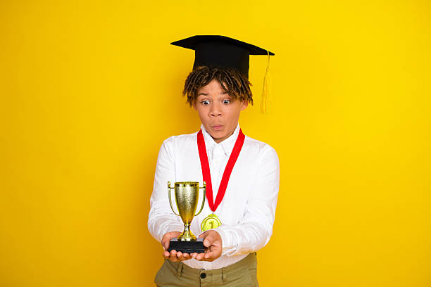 istock Delighted student holding an award trophy with excitement on a bright yellow background emphasizing academic success 2223180676