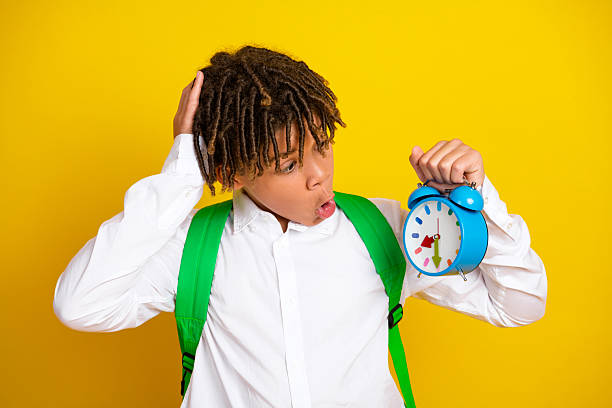 istock Surprised schoolboy with backpack and clock expressing surprise against bright yellow background, symbolizing punctuality 2223180728