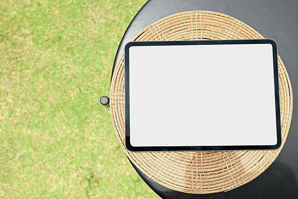 A tablet is sitting on a wicker plate on a table. The tablet is empty and the table is surrounded by grass