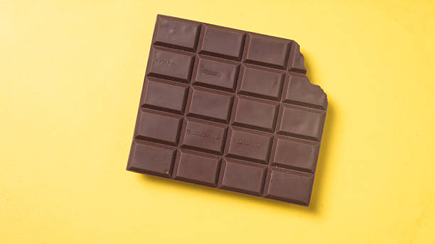 istock A bitten dark chocolate bar with neatly divided squares placed on a bright yellow background, creating a bold and delicious contrast 2223188529