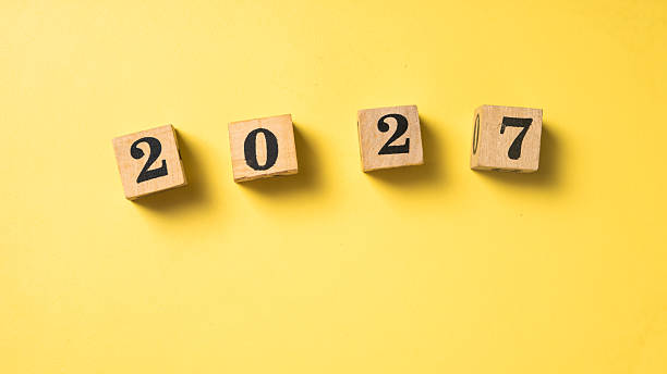 istock Wooden blocks with black numbers forming 2027 arranged in a row on a solid bright yellow background. Symbolizing future year, new beginnings, or goal setting 2223192187