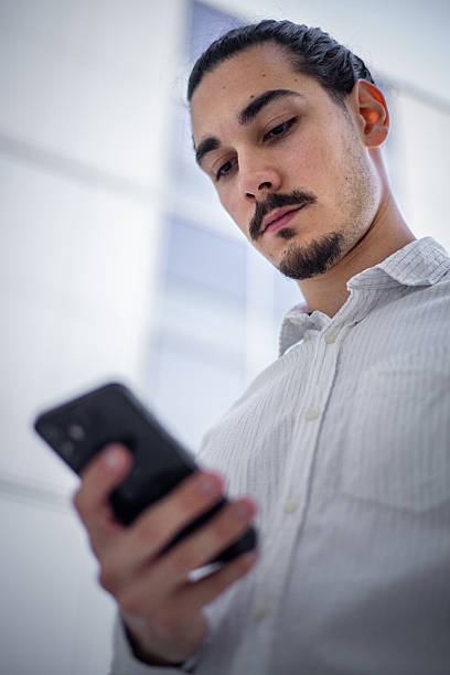 istock Young professional standing in front of a brightly lit office building, checking emails on his phone 2223194788