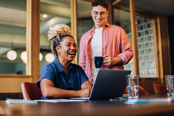 istock Smiling colleagues discussing work at a desk with a laptop and coffee 2223201275
