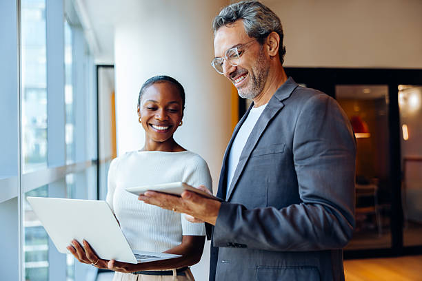 Smiling business professionals sharing ideas while working with laptops and tablets