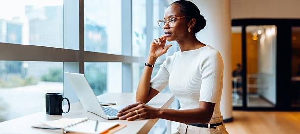 istock Professional woman working on her laptop while standing near large office windows 2223202689