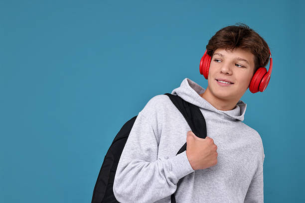 istock Teenage boy in headphones with backpack on light blue background, space for text 2223204571