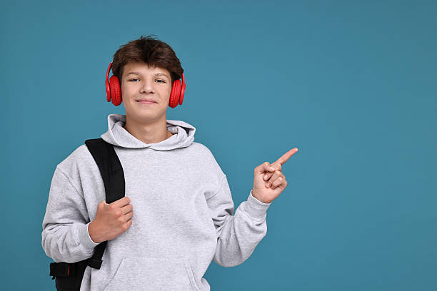 istock Teenage boy in headphones with backpack on light blue background, space for text 2223204766