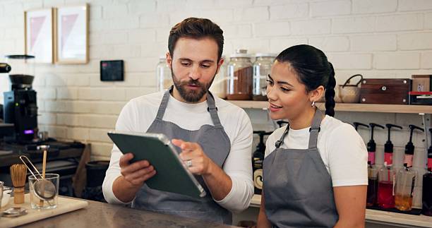 istock Man, waitress and meeting on tablet at cafe of menu update, online orders and inventory management. People, digital and website reviews, stock information and checklist advice of hospitality industry 2223206607
