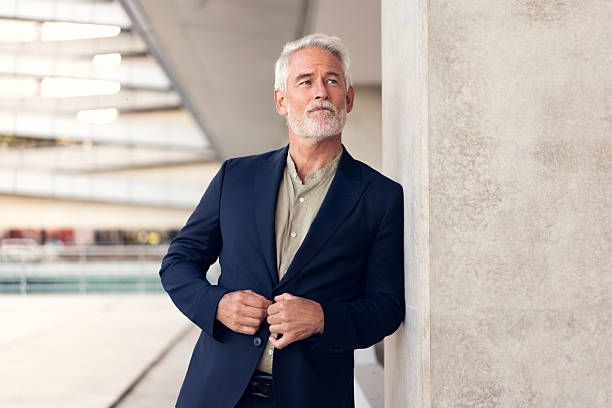 istock Senior businessman adjusting suit while leaning on concrete wall 2223213347