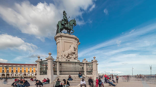 Praca do Comercio (Commerce Plaza). Statue of King Jose I timelapse hyperlapse. The king is symbolically crushing snakes on his path. Cloudy sky and colorful houses on a background. Lisbon, Portugal.