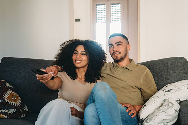 istock Young couple watching television sitting on sofa at home 2223218240