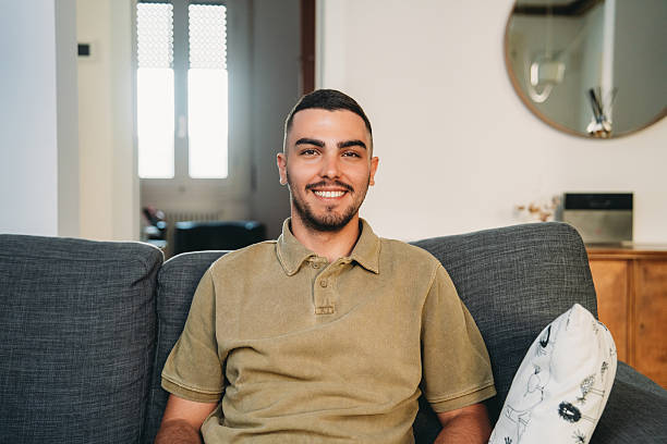 istock Young man smiling and sitting on a couch at home 2223218244