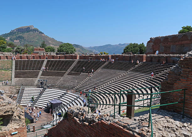 Taormina, Sicily, Italy, June 21, 2025. Steep banked curved seating for large ruined ancient Roman Greek amphitheatre. Incidental people tourists of visitors. Sunny summer day outdoors.