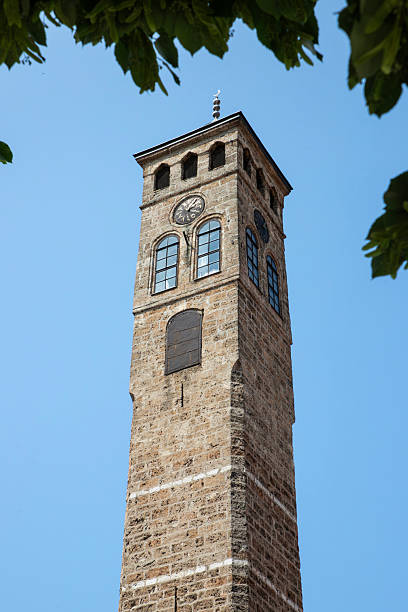 istock Historic Clock Tower Against a Clear Blue Sky Framed by Green Leaves.Sarajevo Uhrturm(Clock Tower) 2223220056