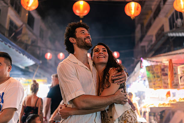 A loving couple stands close together in Bangkok’s Chinatown, smiling warmly as they gaze upward, sharing a joyful moment.