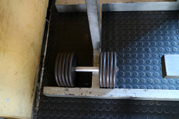 A heavy dumbbell rests on a rubber gym floor, surrounded by metal gym equipment.
