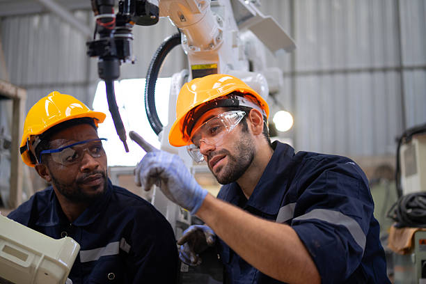 istock Blue collar workers at machine shop with welding robot arm. 2223225567