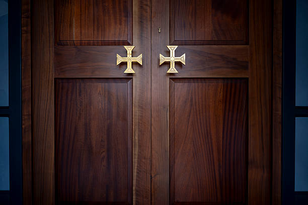 A pair of closed wooden double doors featuring brass handles, set against a dark background. The doors have a classic design, suggesting elegance and security. The lighting is dim, creating a mysterious or solemn atmosphere. Potential use could include interior design inspiration, architectural studies, or thematic storytelling.
