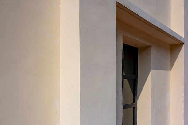 A close-up view of a window set within a beige wall, showcasing architectural detail and texture. The scene is simple yet elegant, with a focus on clean lines and minimalistic design. The image conveys a sense of calmness and modernity, suitable for use in architecture, interior design, or minimalist art contexts.