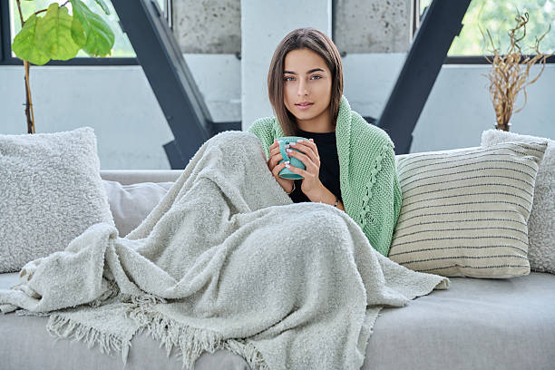 istock Beautiful young woman sitting under warm blanket with cup in her hands, on sofa 2223226888