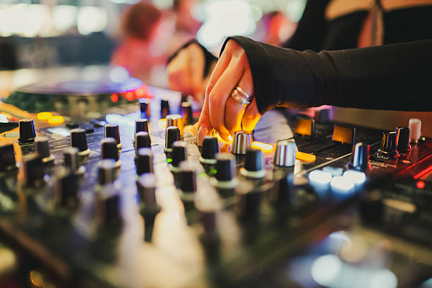 DJ adjusting knobs on professional audio mixer at live music event with vibrant lights, capturing the energy of nightlife and electronic music performance.
