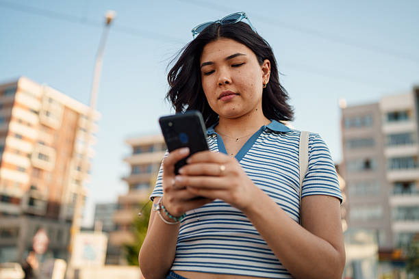 A young woman walking down the street while using her phone, navigating through the urban environment with modern connectivity at her fingertips.