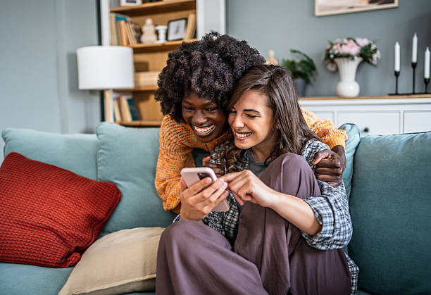 istock Two young women laughing while using a smartphone on the sofa at home 2223246215
