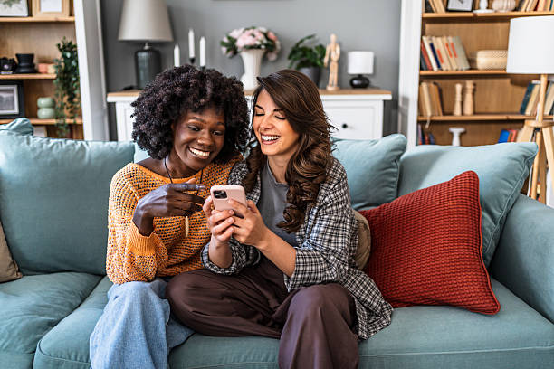 istock Two smiling women sharing a moment of laughter on sofa while using smartphone 2223246748