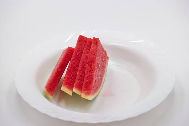 Juicy, vibrant watermelon is neatly cut into slices and arranged on a simple white plate, perfect for a summer picnic or outdoor gathering. The bright red flesh promises refreshing enjoyment.