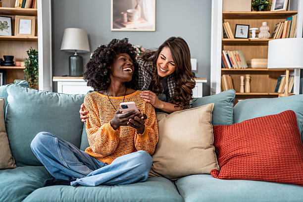 istock Two young women laughing and using a smartphone on the sofa at home 2223247333