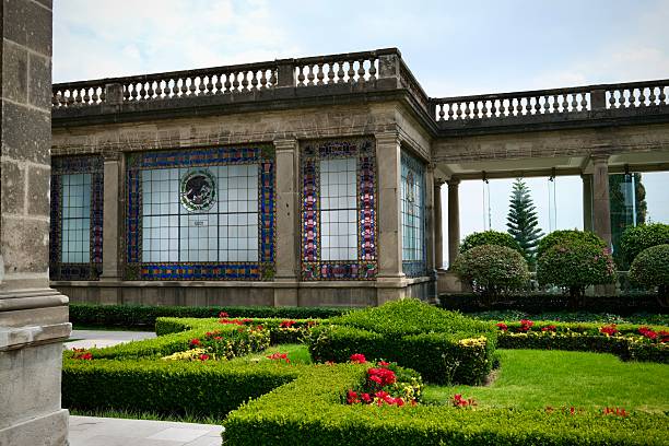 Mexico City, CDMX, Mexico- February 20, 2025: A lush formal garden with bright red flowers set against a stunning stained glass window.