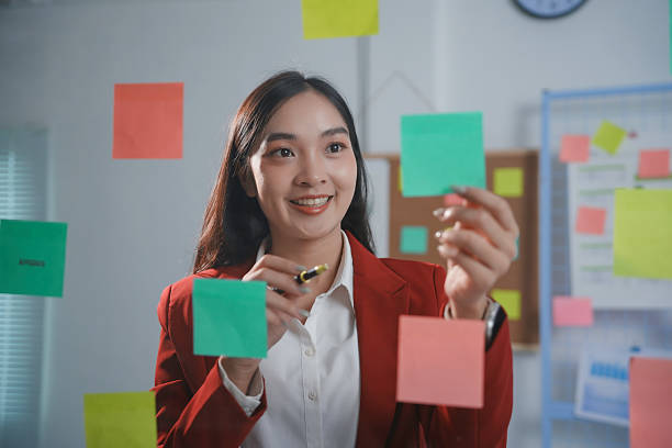 istock Female professional arranging colorful sticky notes on glass wall, organizing workflow with focused energy and strategic planning in modern office setting 2223252362