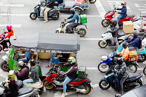 Queued waiting motorcycles and a tuktuk on S Sathorn Road in Bangkok below Sathorn Bridge. People are waiting for green signal and are driving from northern to souther direction. Some drivers are express delivery drivers