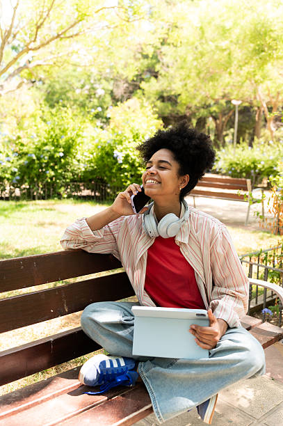 istock Young woman using digital tablet and talking on smartphone in park 2223256314