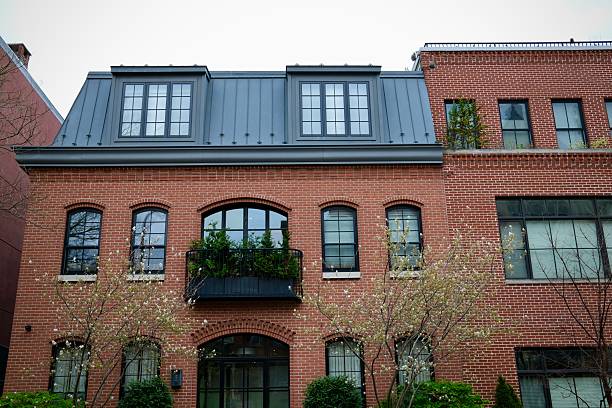 Philadelphia, Pennsylvania, USA- April 15, 2025: A red brick townhouse features black trim and a balcony framed by blossoming spring trees in a quiet residential area.