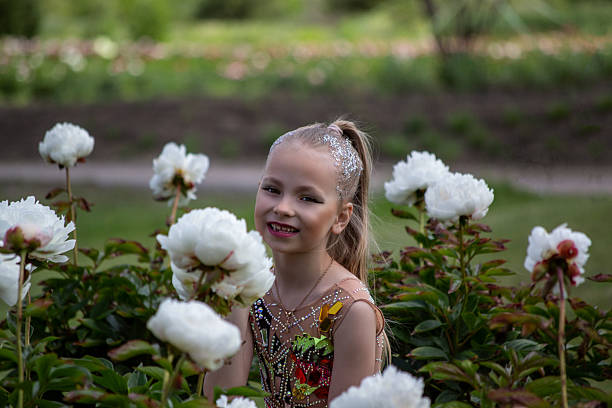 little gymnast in a beautiful swimsuit in a garden with peony flowers