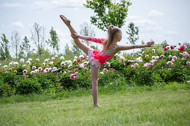 little gymnast in a beautiful swimsuit in a garden with peony flowers